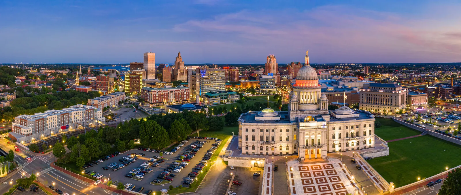 Aerial view of the illuminated Rhode Island state capitol building and city skyline at dusk.