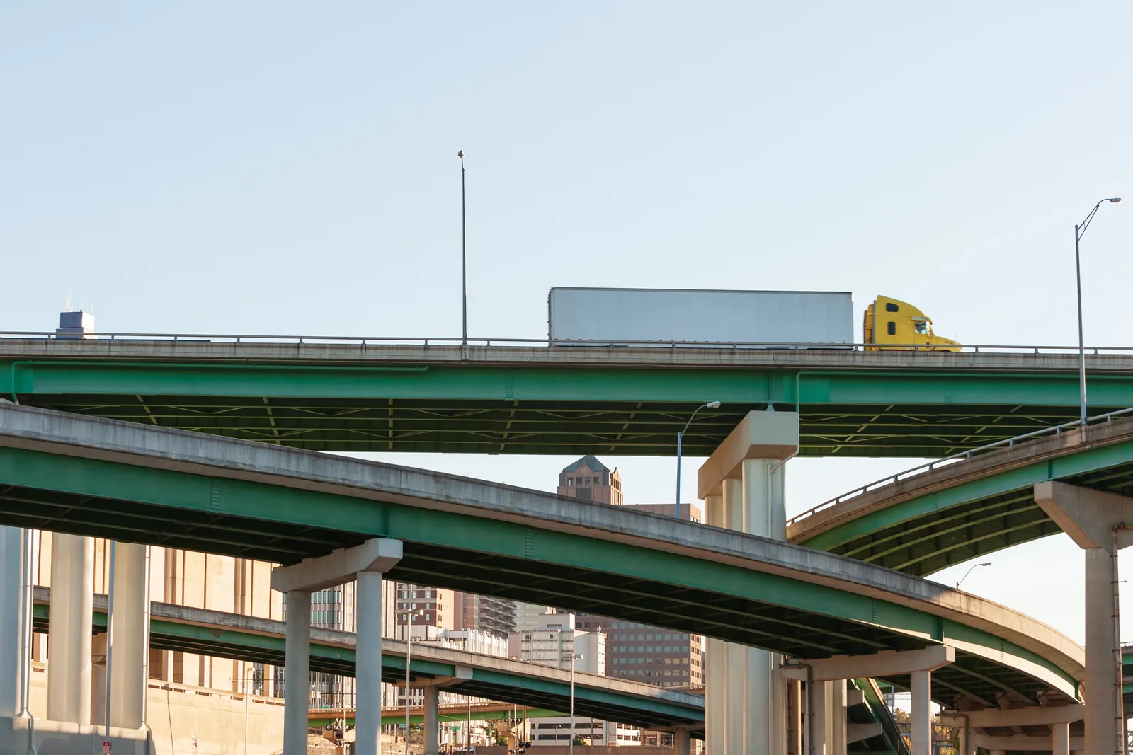 Semi-truck crossing an elevated highway interchange supported by concrete pillars.