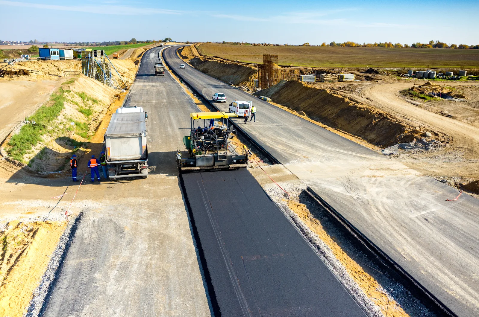 Aerial view of an asphalt paver and construction crew paving a wide road.