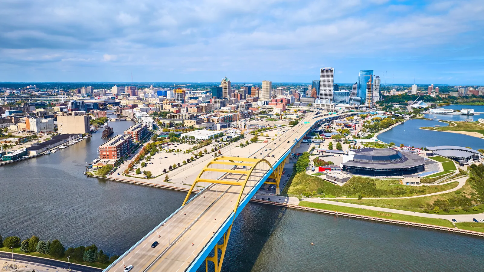 Aerial view of a city skyline with a yellow arched bridge crossing a wide river leading to a bay.