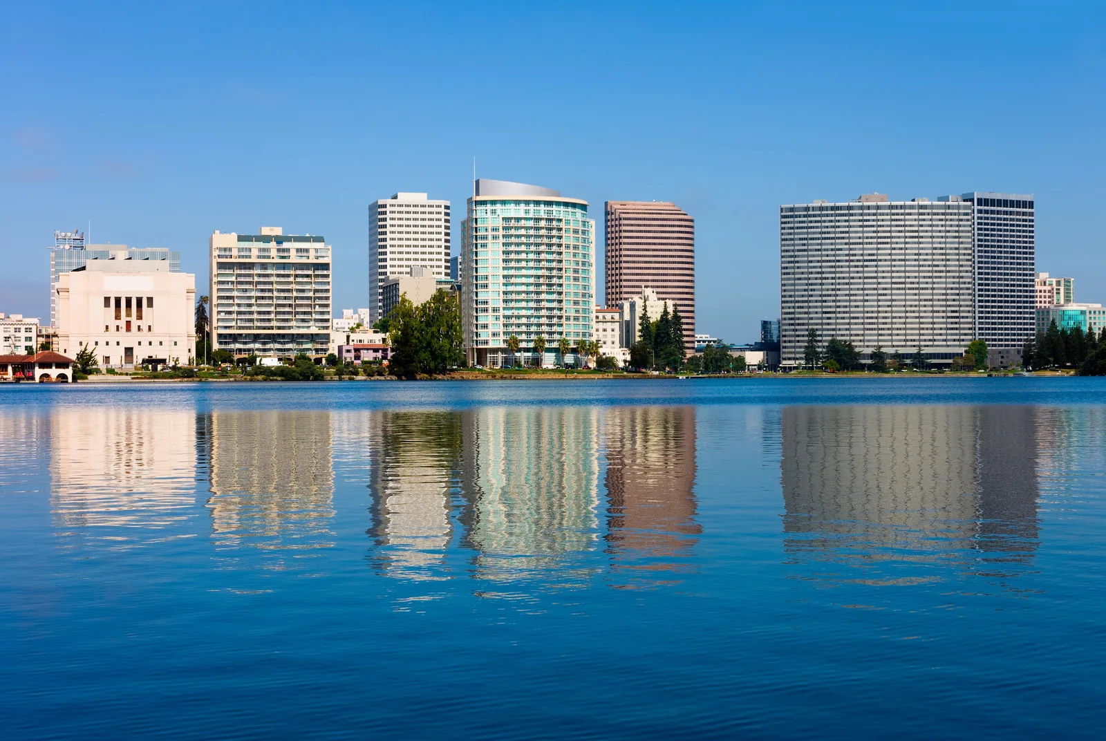 City skyline reflected across calm water under a blue sky.
