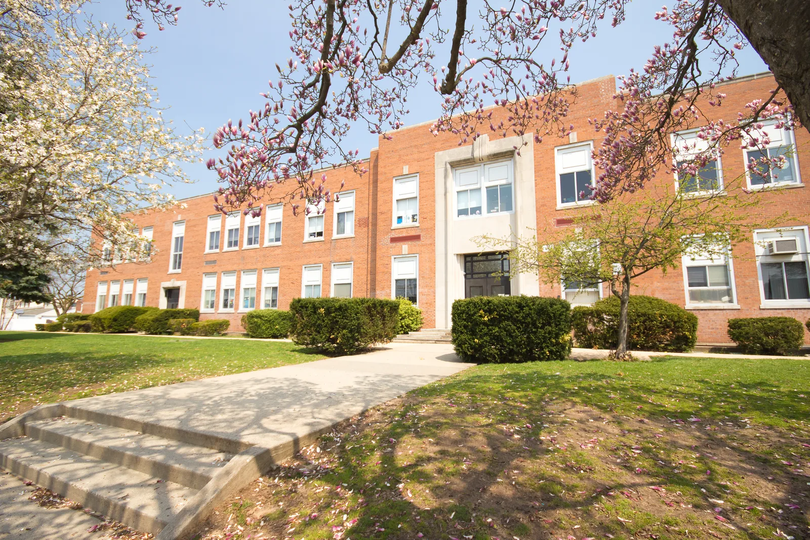 Red brick public school building fronted by a paved walkway and green lawn.