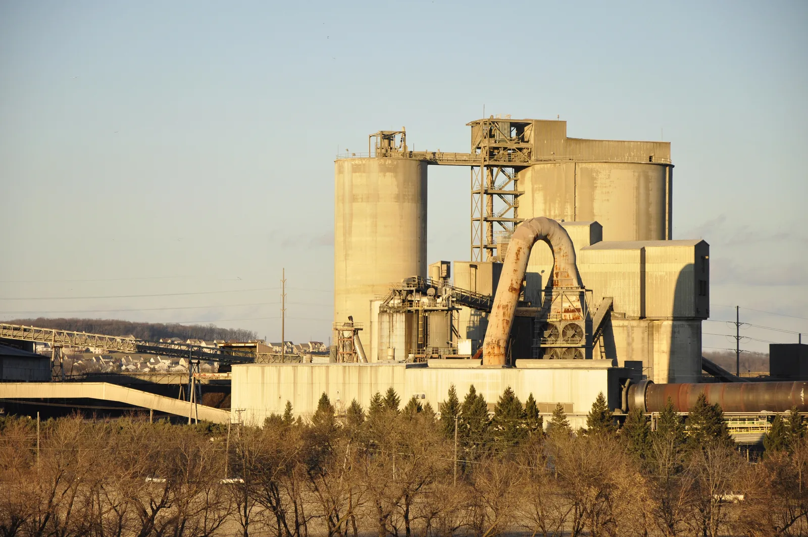 Industrial cement plant with twin concrete silos, a rotary kiln, and conveyor systems.